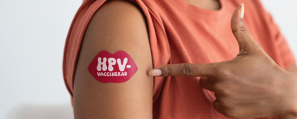 Finger pekar på arm med klistermärke med texten HPV-vaccinerad.