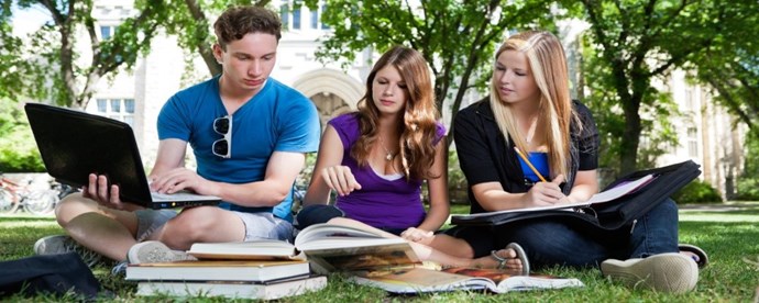 Tre studenter pluggar på gräset i en park